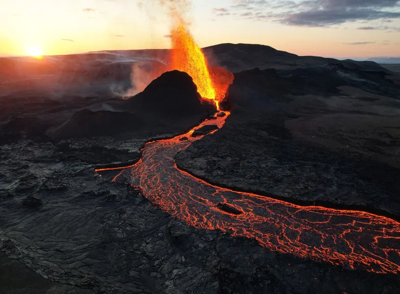 Volcanic eruption with glowing lava flow during sunset