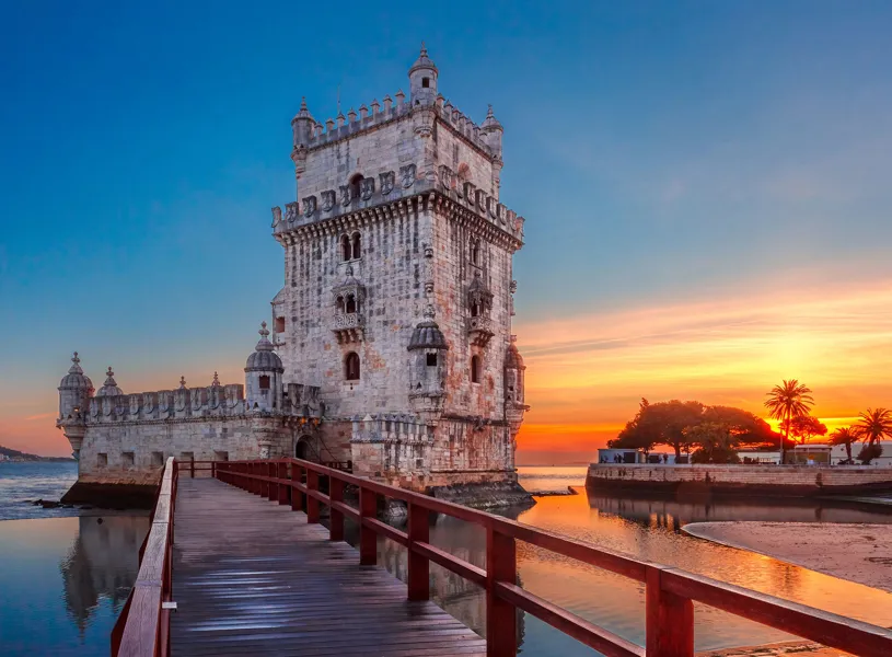 Belém Tower with wooden walkway and calm waterfront at sunset in Lisbon, Portugal
