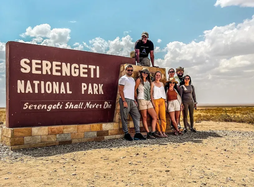 Group of travellers standing in front of the Serengeti National Park sign in the Serengeti, Tanzania