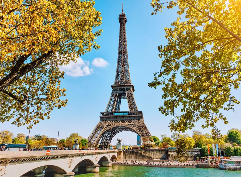 Eiffel Tower framed by trees, bridge and blue sky in Paris, France
