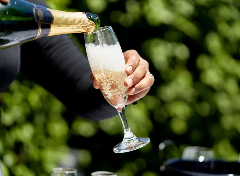 Champagne poured into flute outdoors and blurred greenery background
