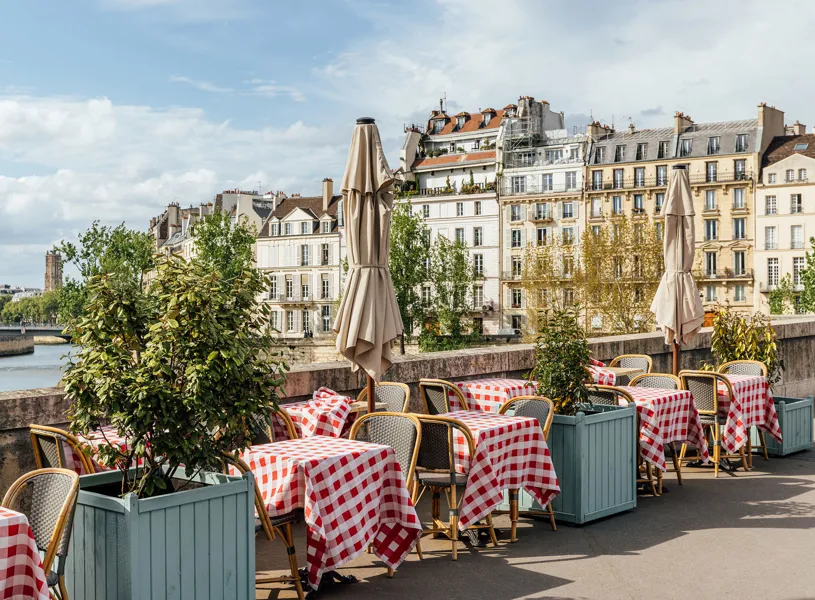 Café with checkered tables, umbrellas, plants on the bank of Seine River