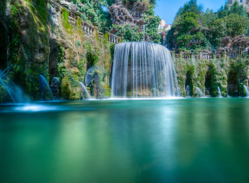 Waterfall cascading into turquoise pool at Villa d’Este gardens in Tivoli