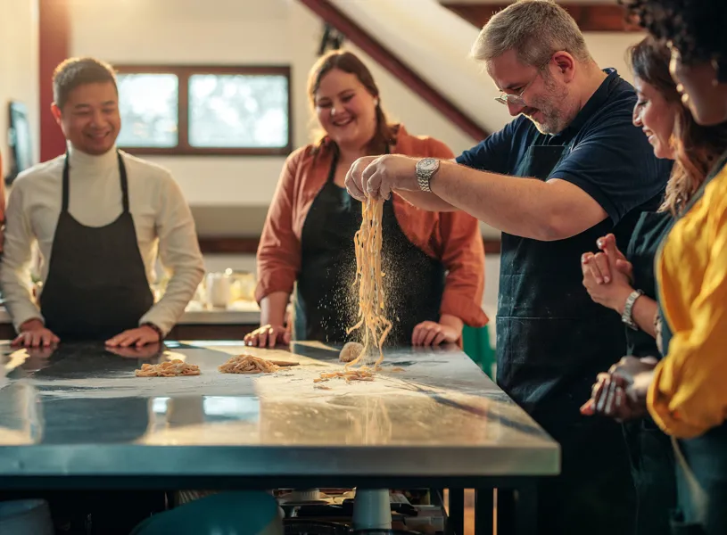 "Hands tossing strands of fresh pasta during cooking class on floured countertop 