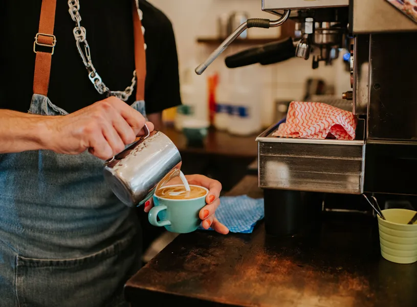 Barista pouring milk into cup to create latte art