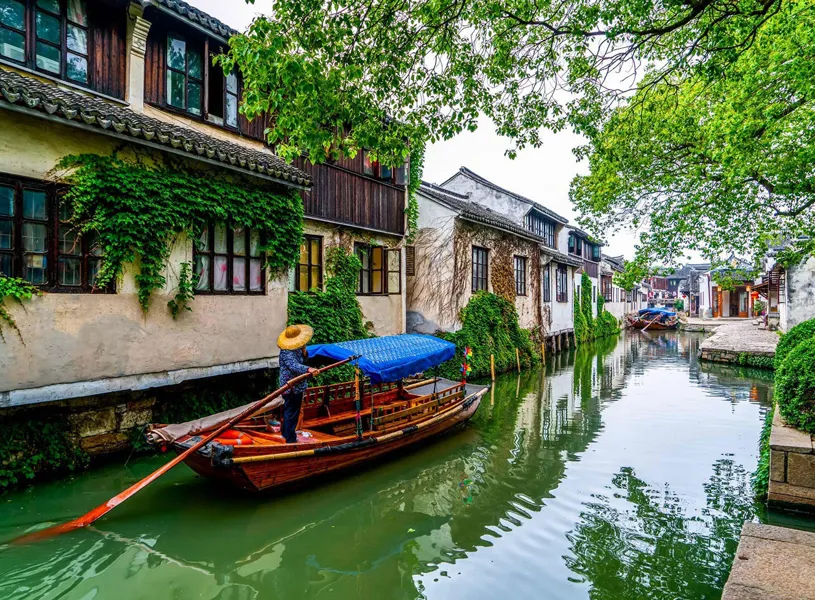 Green canal with traditional houses and a boatman, China 