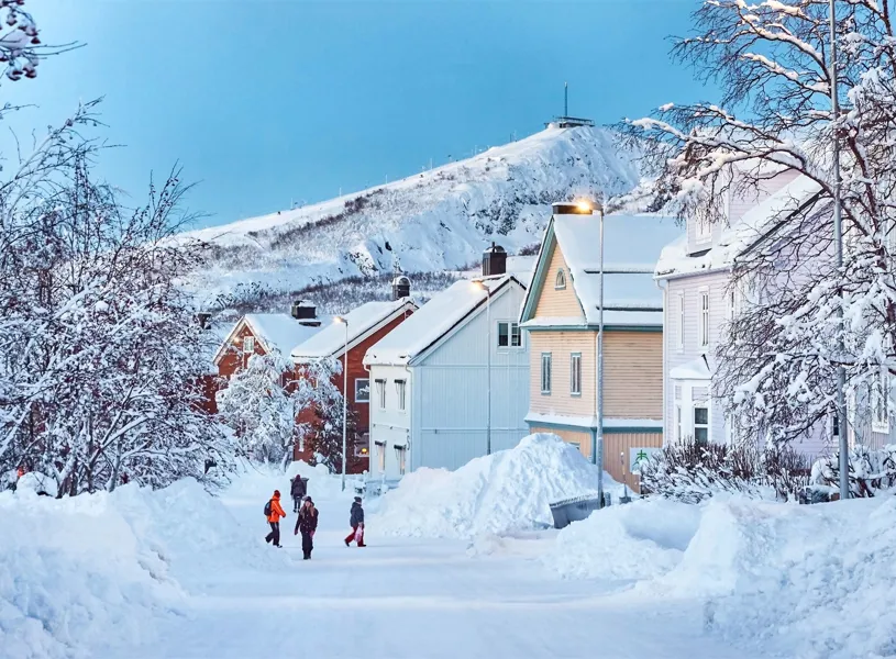 Snow-covered street with colourful houses and mountain backdrop in Kiruna, Sweden