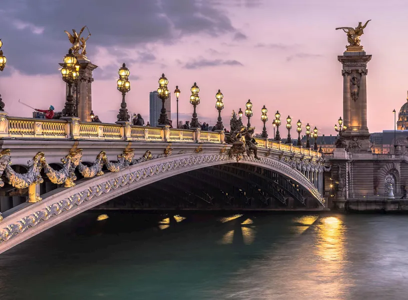 External view of a bridge illuminated by ornate lampposts and sculptures in Paris, France