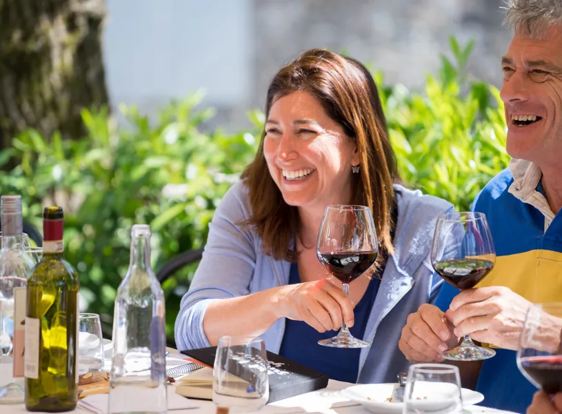 A smiling couple dining outdoors with red wine glasses
