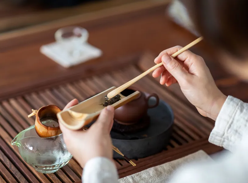 Hands preparing loose leaf tea with bamboo scoop and stick, wooden tray, Beijing, China