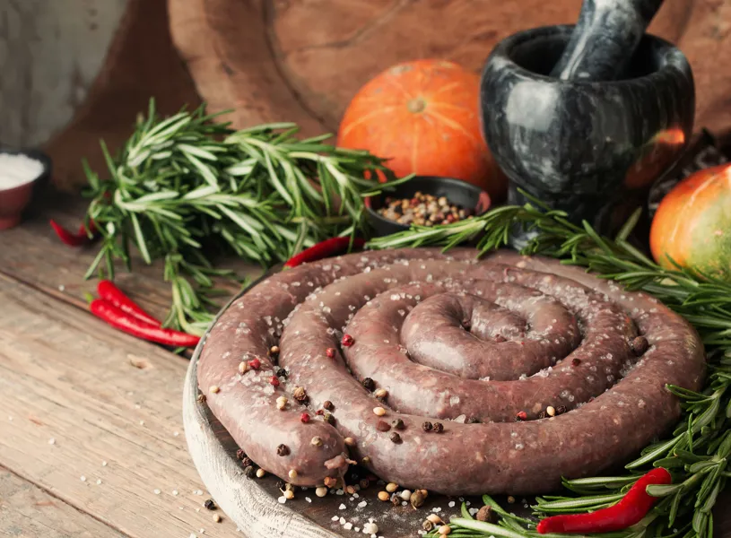 Coiled sausage with rosemary and chilli peppers on wooden board, South Africa 