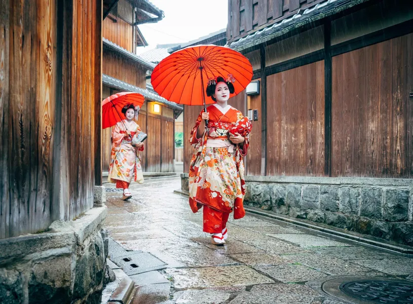 Maiko women with red umbrellas walking along paved street in Kyoto, Japan