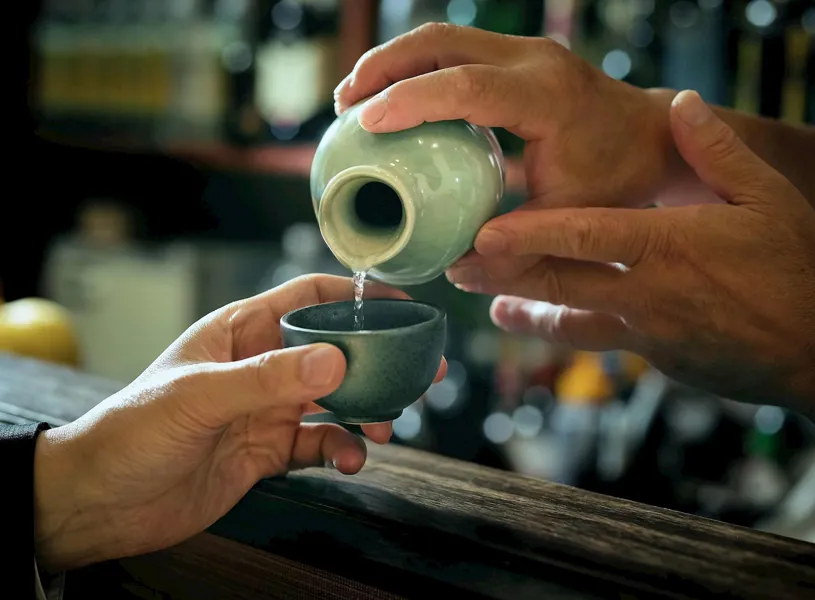 Close up of sake being poured from a ceramic flask into a small cup, Japan