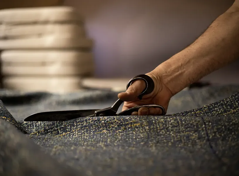 Hand with scissors cutting tweed fabric, Edinburgh, Scotland