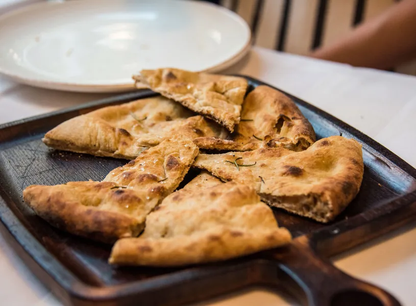 Close up of sliced flatbread on a serving wooden cutting board with handle, in a restaurant in Tirana, Albania