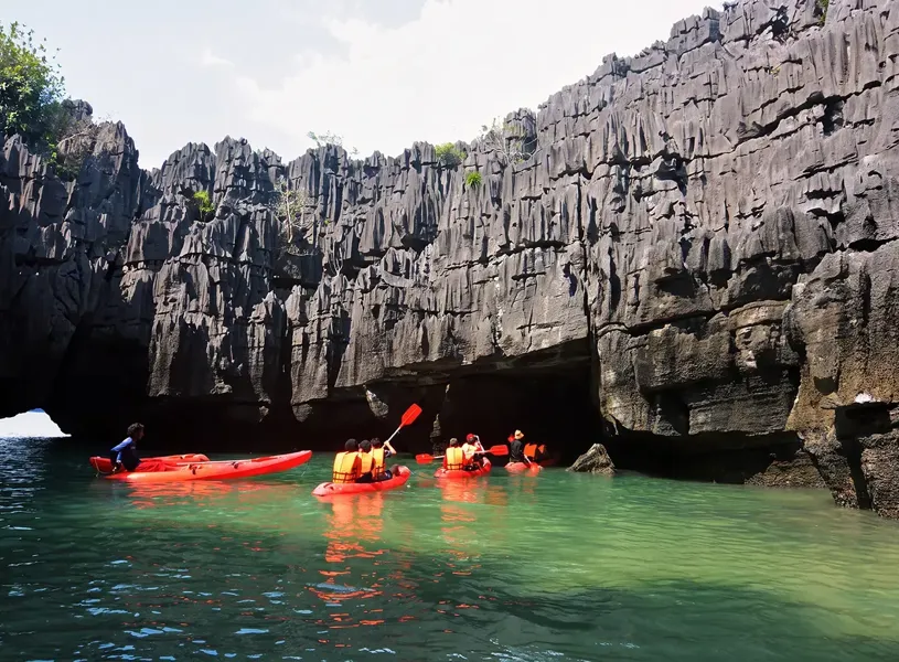 People Kayaking on water sounded by dramatic rock cliffs in Ho Ba Ham, Vietnam